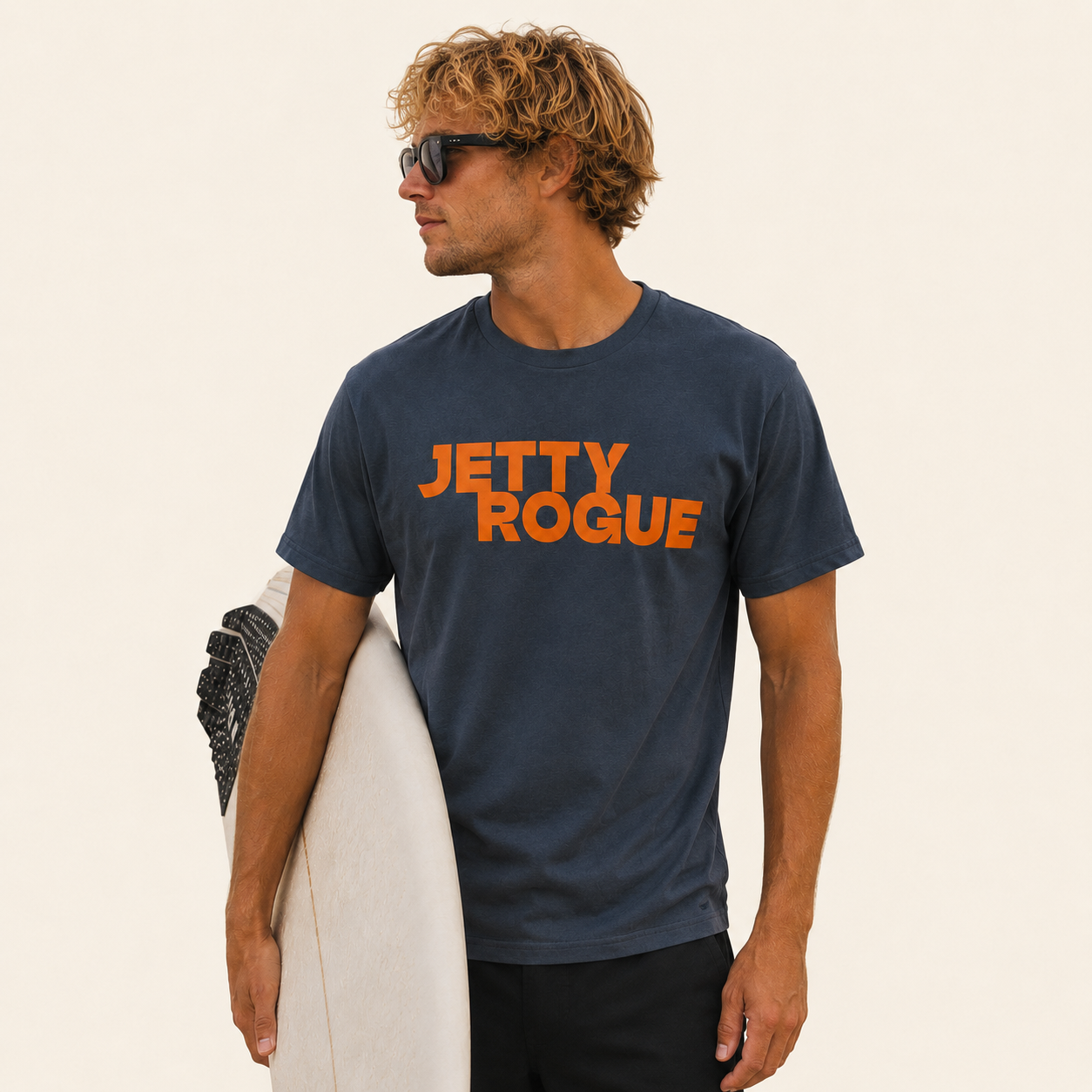 Petrol blue tee on model: Jetty Rogue unisex tee in petrol blue with burnt orange logo, relaxed fit, male model holding surfboard
