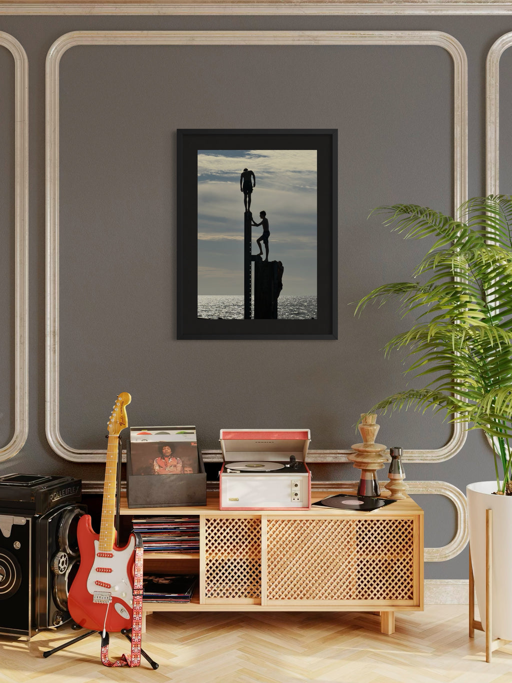 Framed artwork above a wooden cabinet with a guitar and records, against a gray wall with decorative molding.