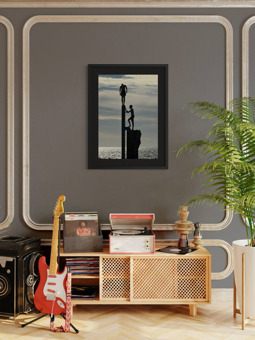 Framed artwork above a wooden cabinet with a guitar and records, against a gray wall with decorative molding.