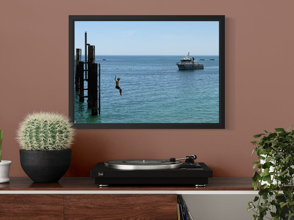 Framed picture of a person diving into water with a boat, displayed on a wall above a turntable.