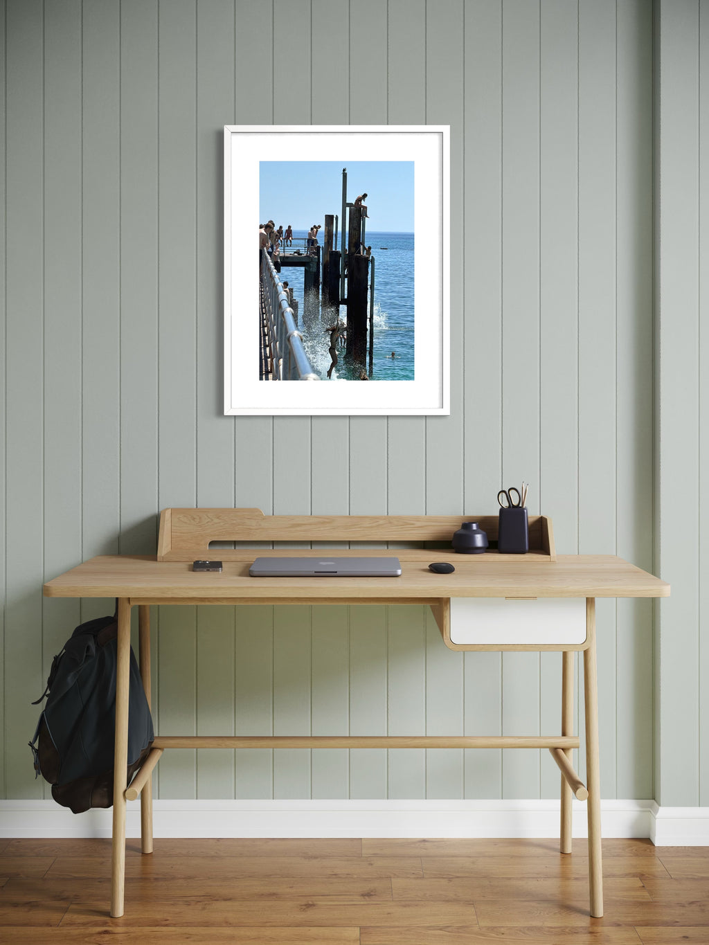 Wooden desk with a framed picture of a dock on a gray wall.
