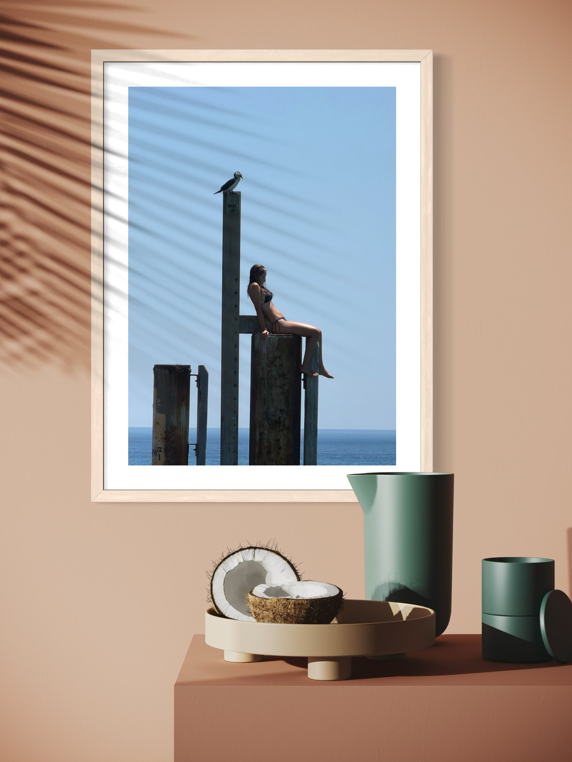 Framed artwork of a woman sitting on a dock with a blue sky, placed on a beige surface with decorative items.