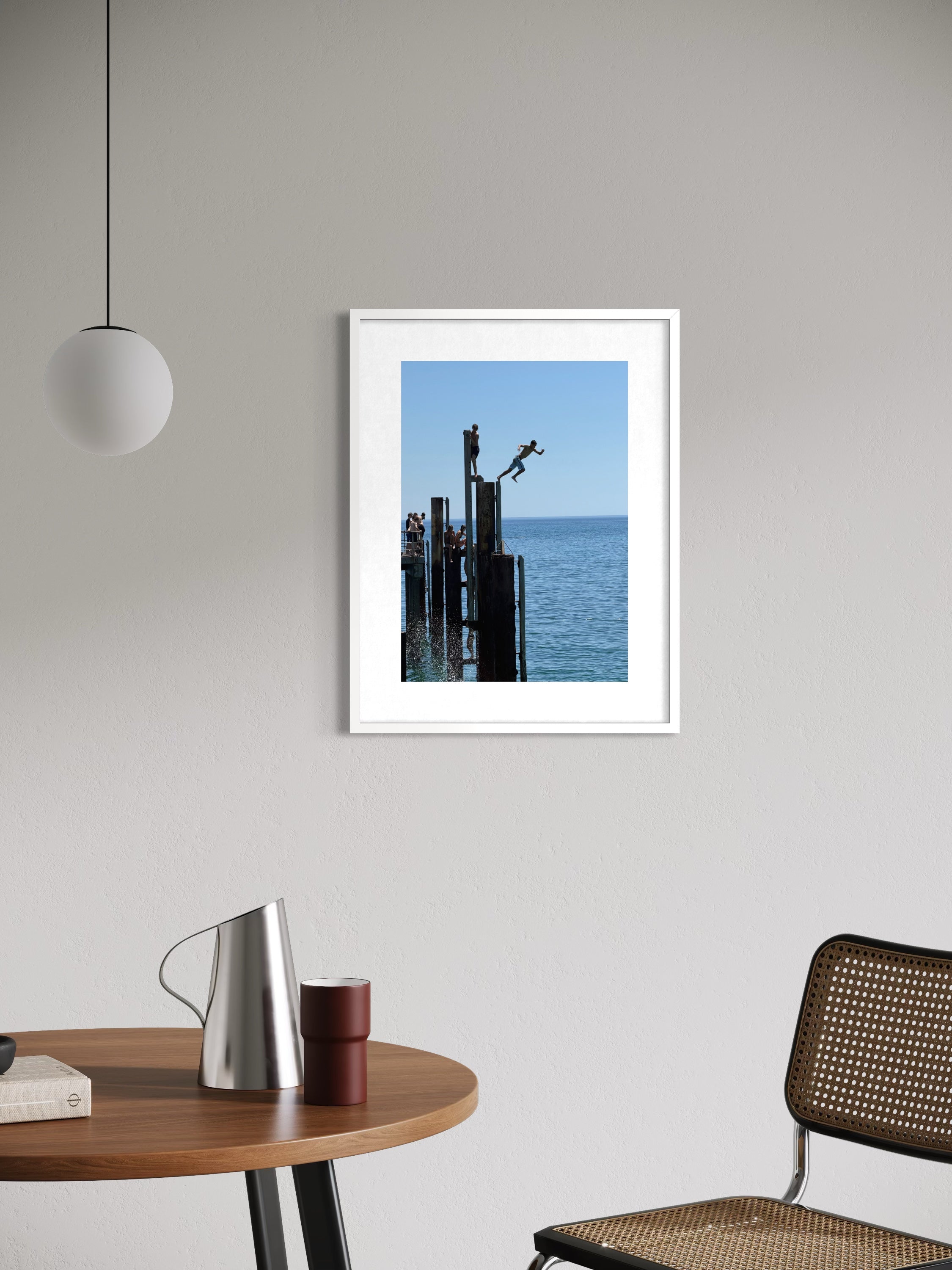 Framed artwork of a pier scene on a wall above a table and chair.