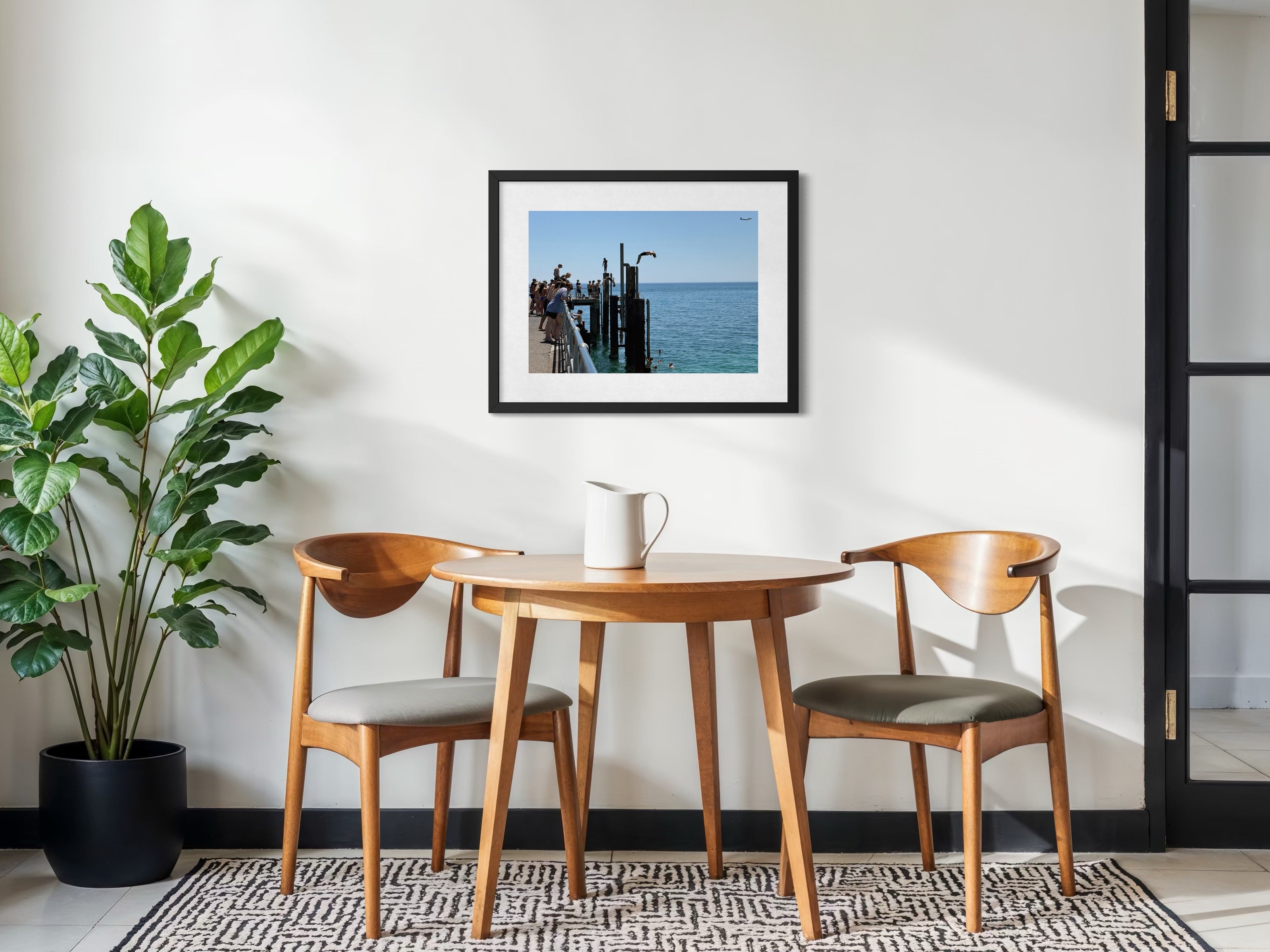 Dining area with wooden table and chairs, plant, and framed picture on wall.